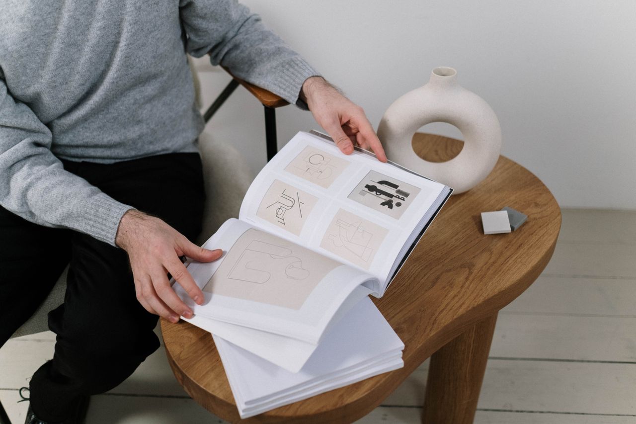 A man flips through pages of a design portfolio on a wooden table in modern style.
